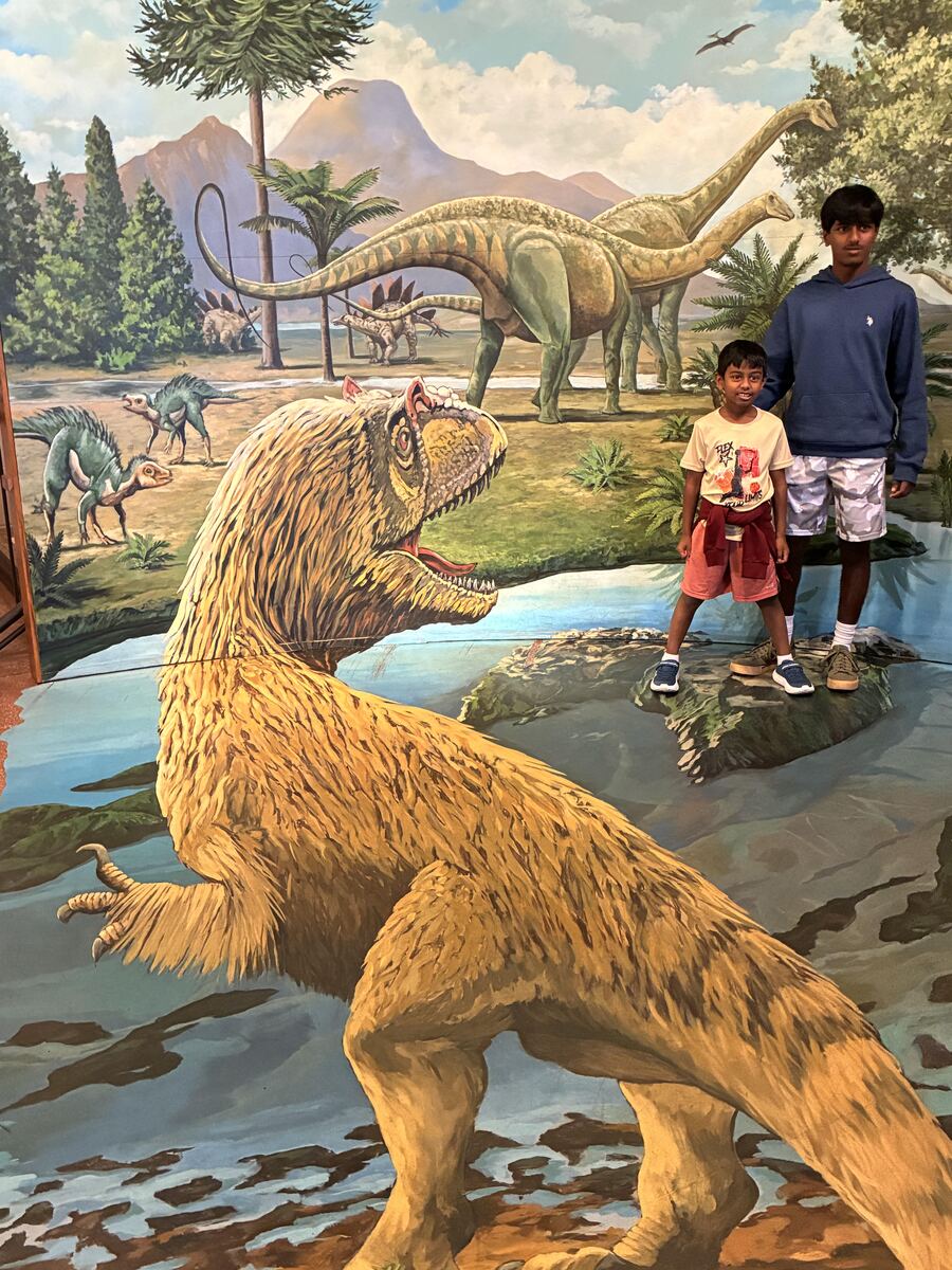 Sanjeeva and Nidhulan posing in front of a dinosaur mural