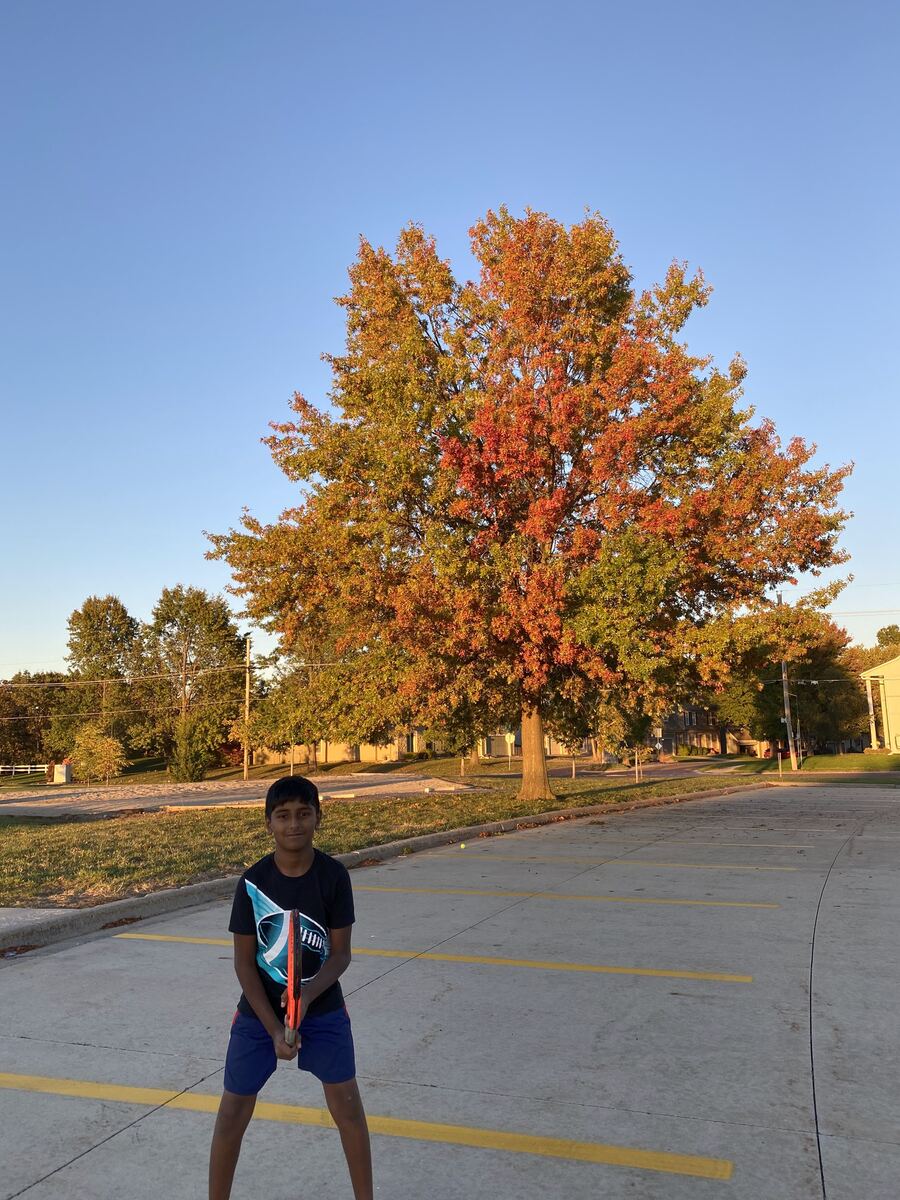 Young Sanjeeva holding his racket in front of a bright orange fall tree